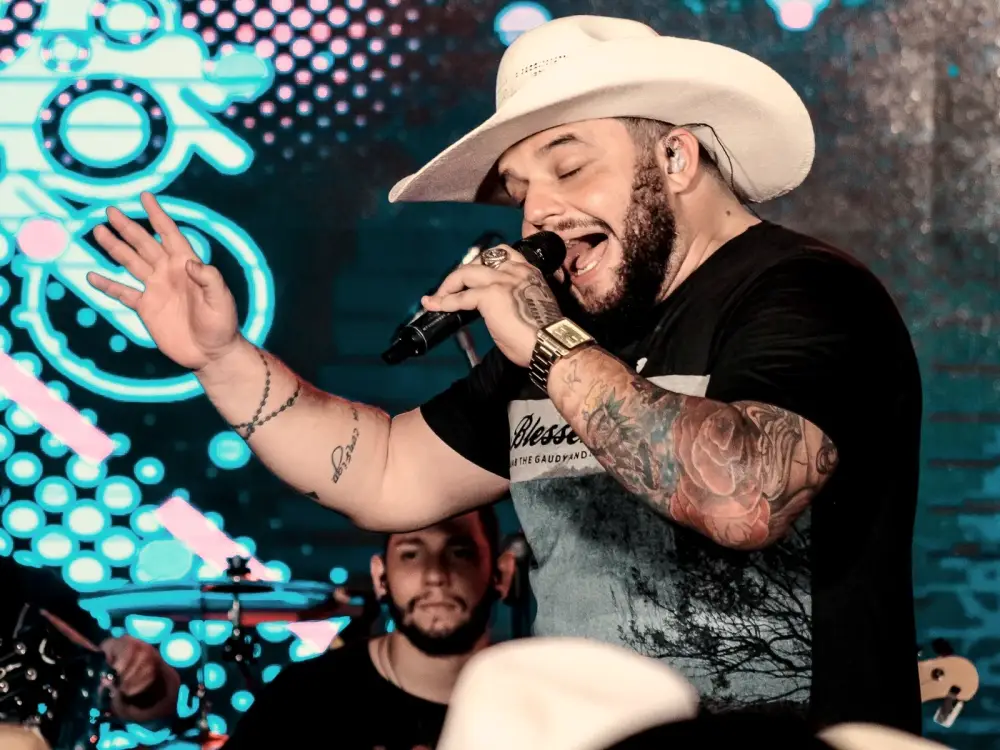 Cadu cantando ao microfone com chapéu branco